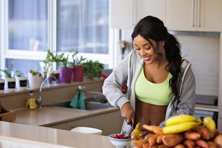 Smiling woman preparing fresh fruit in a sunlit kitchen, embodying a healthy lifestyle.