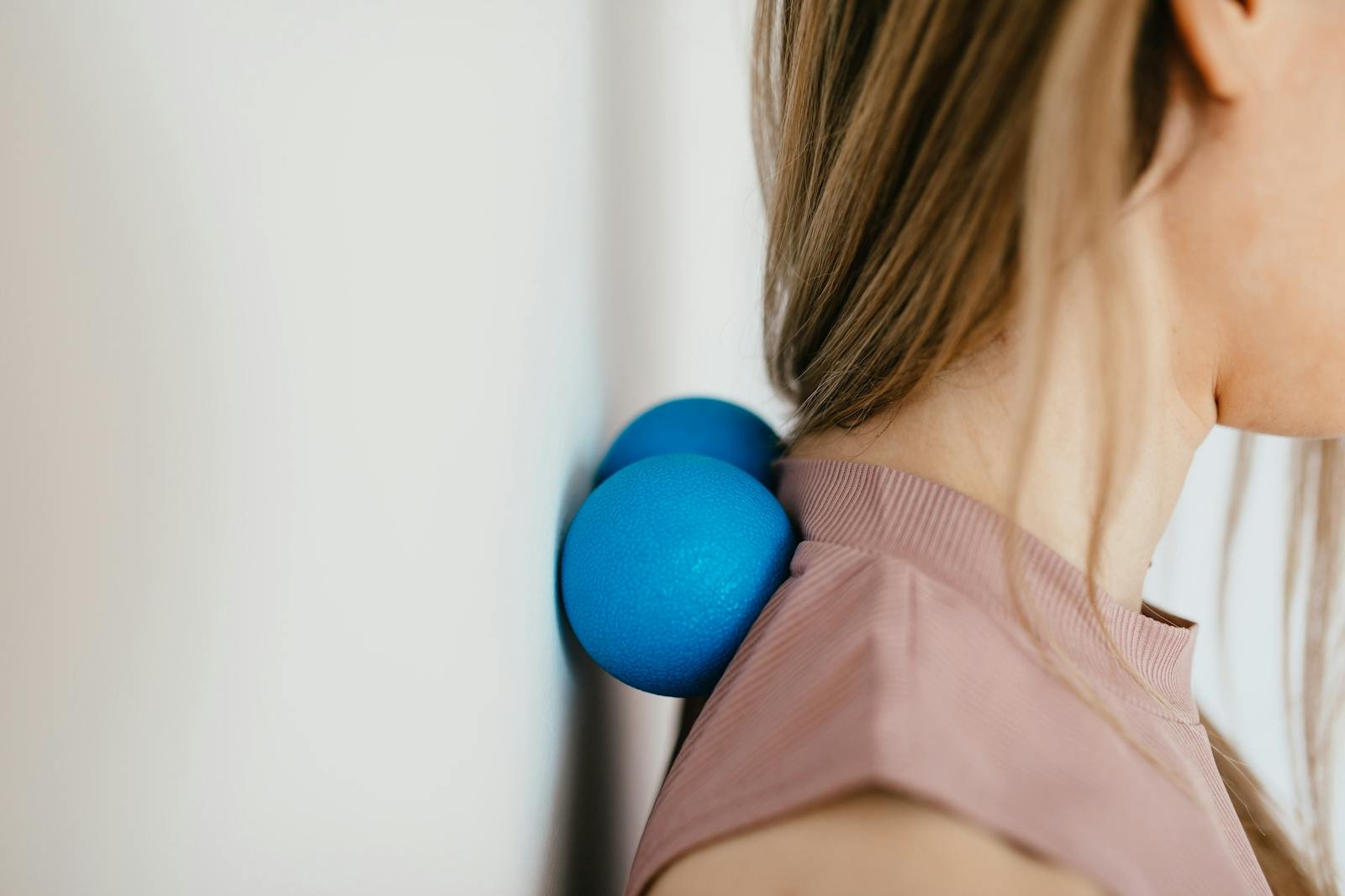 Close-up of woman using blue massage balls for neck relief against a wall.