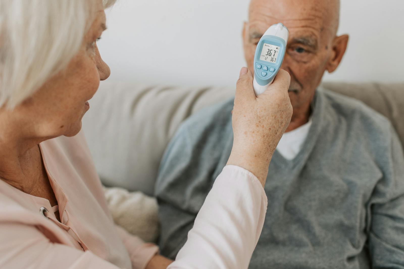 An elderly woman checks the temperature of a senior man using a digital thermometer indoors.