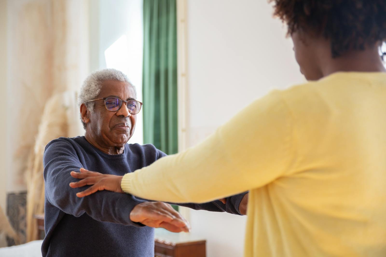 An elderly man with a caregiver assisting him in exercise at home.