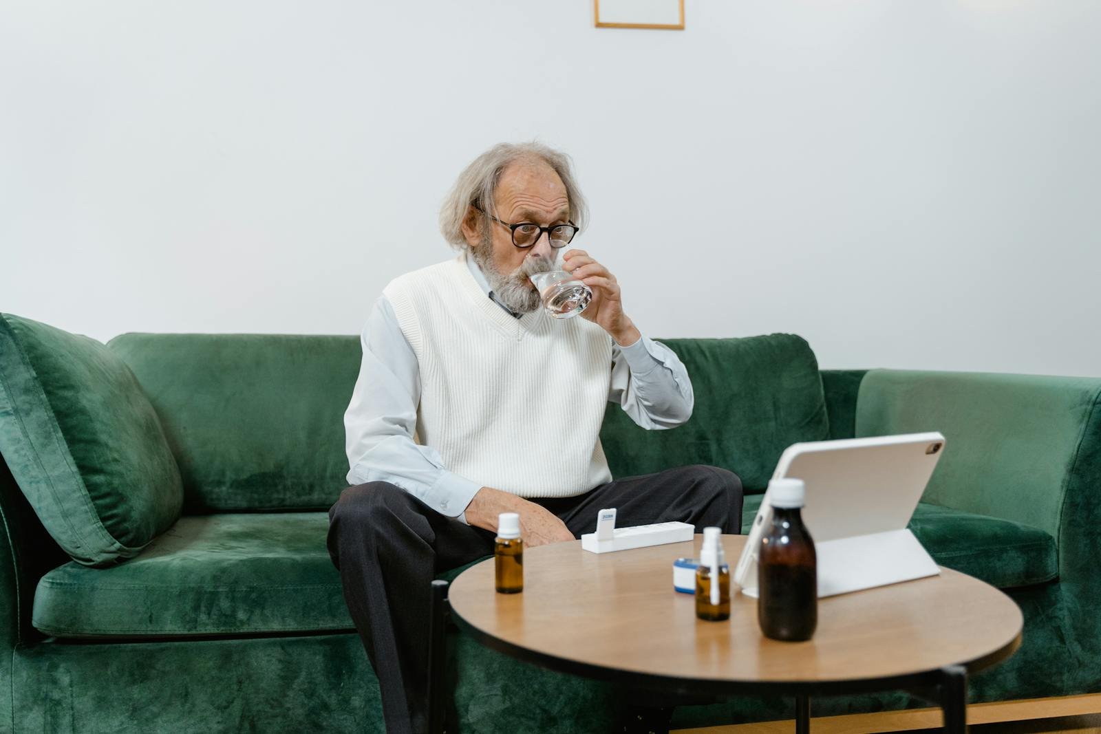 Elderly man using telehealth services with medicine and water indoors.