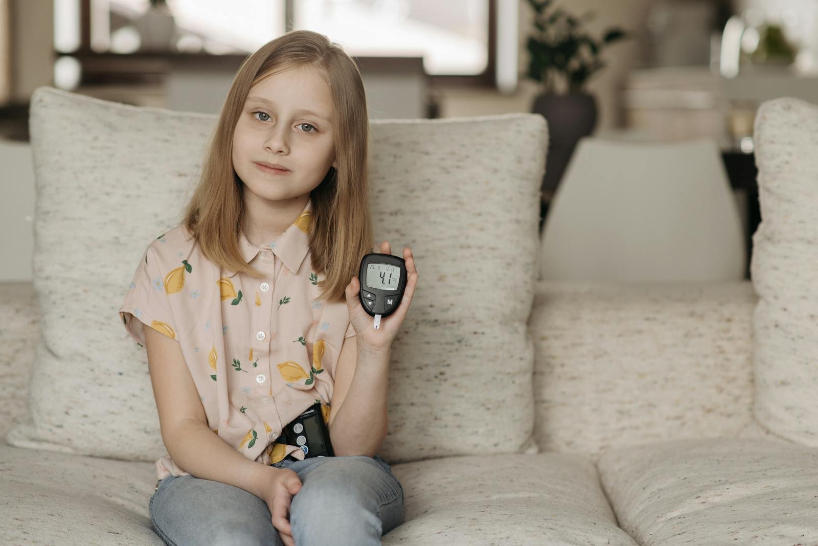 A girl sitting on a couch displaying a glucometer, highlighting health awareness.